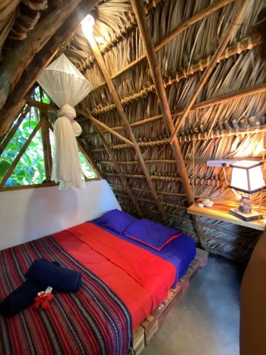 a bed in a thatched room with a window at Caracolito Hostal in Las Peñitas