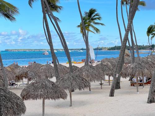a beach with some straw umbrellas and palm trees at STUDIOS WITH POOL VIEW - SOL CARIBE TROPICAL - playa LOS CORALES in Punta Cana