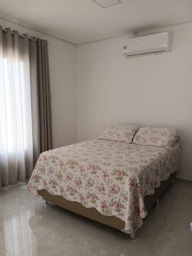 a white bedroom with a bed with a floral blanket at Refúgio do Mar in Japaratinga