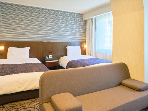a hotel room with two beds and a couch at APA Hotel Matsuyamajo Nishi in Matsuyama