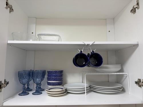 uma prateleira branca com pratos, taças e copos em Casa azul - próx de Nazaré com Split e Wi-Fi em Belém