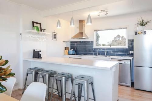 een keuken met een wit aanrecht en 4 krukken bij Aldinga Beach Breakaway - C21 SouthCoast Holidays in Aldinga Beach