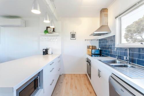 een keuken met witte werkbladen, een wastafel en een raam bij Aldinga Beach Breakaway - C21 SouthCoast Holidays in Aldinga Beach