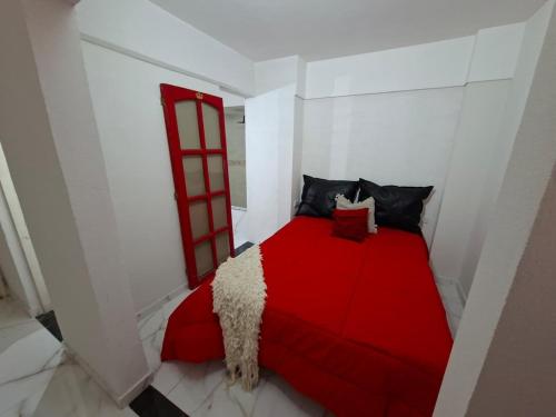 Una cama roja en una habitación blanca con una ventana roja. en Departamento Vicco, en Pinamar
