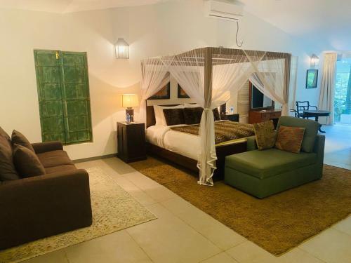 1 dormitorio con cama con dosel, sofá y silla en Rain Drops Wellness Villa Sinharaja, en Mederipitiya