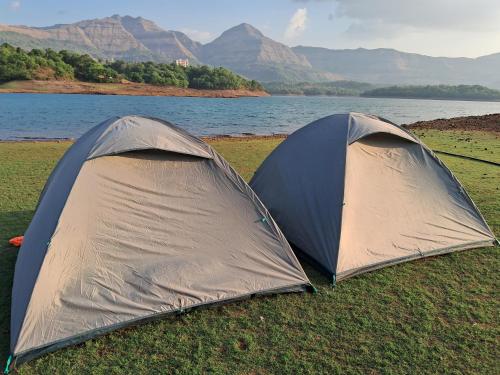 班达尔达拉Bhandardara I land Camping的两顶帐篷搭在水体附近的草地上。
