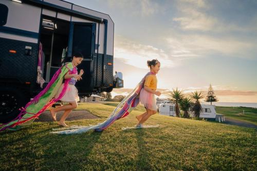 two children running with kites in front of a rv at Tasman Holiday Parks - Papamoa Beach in Papamoa