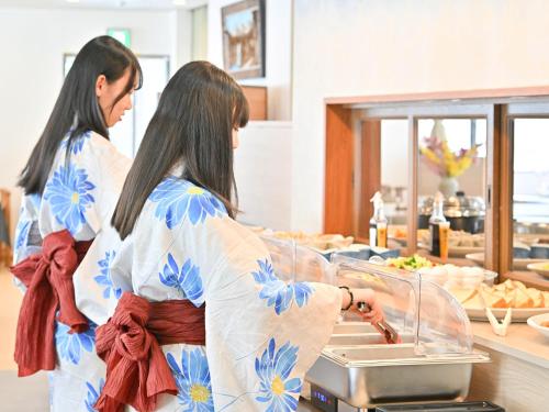 dos mujeres de pie en una cocina preparando comida en Komakusa Hotel, en Matsumoto