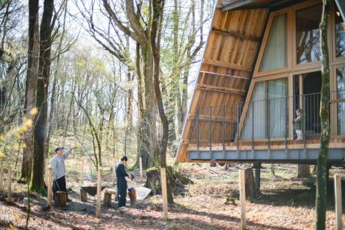 a treehouse in the woods with people standing in front of it at SANU 2nd Home 北軽井沢 1st in Naganohara
