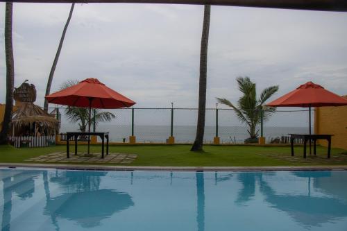 a swimming pool with two umbrellas and the ocean at Laguna Beach Garden in Uswetakeiyawa