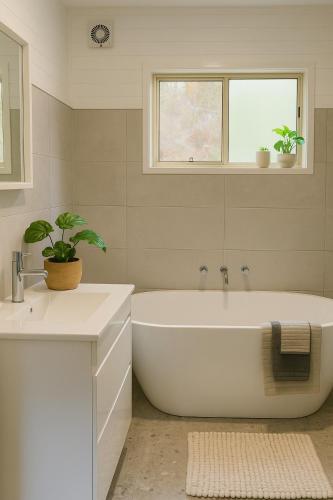 a white bathroom with a tub and a sink at Cocora Beach Cottage - pet friendly in Eden
