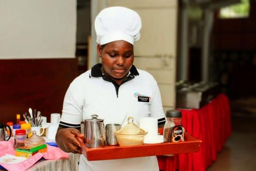 a chef holding a tray of food at Psalms Motel in Entebbe