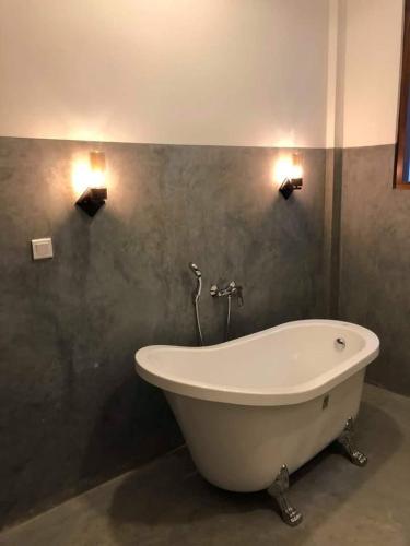 a bath tub in a bathroom with two lights on the wall at Villa Coconut Tree in Angulugaha