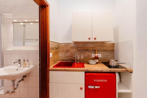 Kapitaenshaus-Lassen-Zimmer-Santa-Maria في فيسترلاند: مطبخ صغير مع حوض وخزانة حمراء