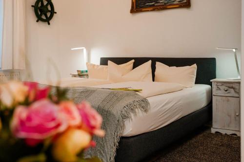 Kapitaenshaus-Lassen-Zimmer-Santa-Maria في فيسترلاند: غرفة نوم مع سرير مع ملاءات بيضاء وورود وردية