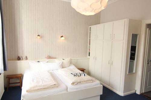 Kapitaenshaus-Lassen-Zimmer-Amistad في فيسترلاند: غرفة نوم بها سرير أبيض ووسائد بيضاء وثريا