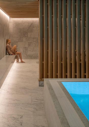 a woman sitting on a bench next to a swimming pool at Skostredet Hotel & Spa in Bergen