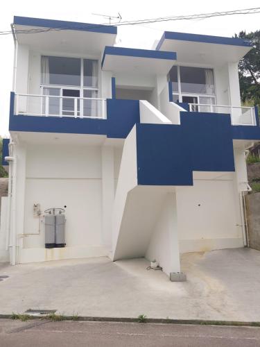 a white house with a blue staircase on it at ペンションsakuraRIGHT in Motobu