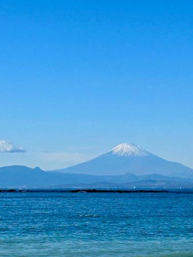 a snow covered mountain in the distance over the water at Cielito Hayama 最大10名 海まで10分 テラスBBQ 葉山の空と海と富士山に出会うヴィラ in Hayama