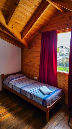 Una cama en una habitación de madera con ventana. en Cabañas Matices, en El Calafate
