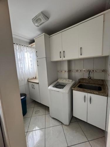 una pequeña cocina con armarios blancos y lavadora en Apto a 80 metros do mar para 8 pessoas, en Itapema