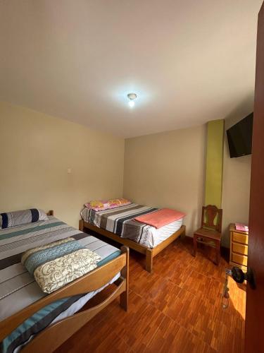 ルナウアナにあるHospedaje Cesarのベッド2台、テレビ、椅子が備わる客室です。