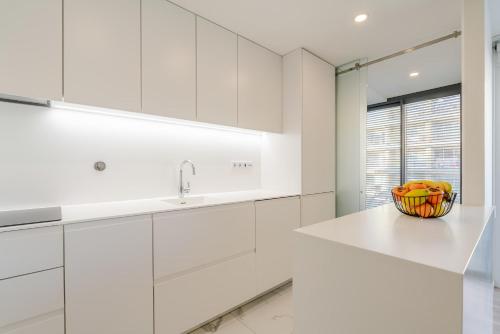 a white kitchen with a bowl of fruit on a counter at Spacious Light-Filled Flat with Garage by HostWise in Leça da Palmeira