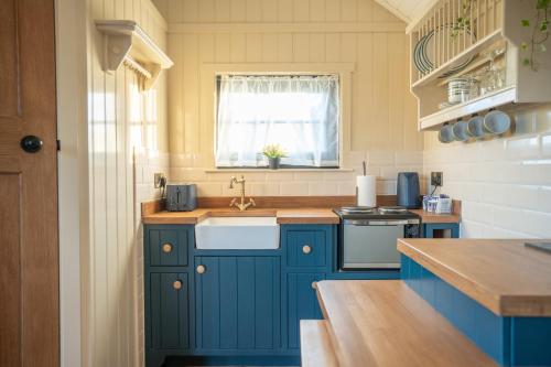 eine Küche mit blauen Schränken, einem Waschbecken und einem Fenster in der Unterkunft Friels Fairy Tree Hawthorn lodge in Swatragh