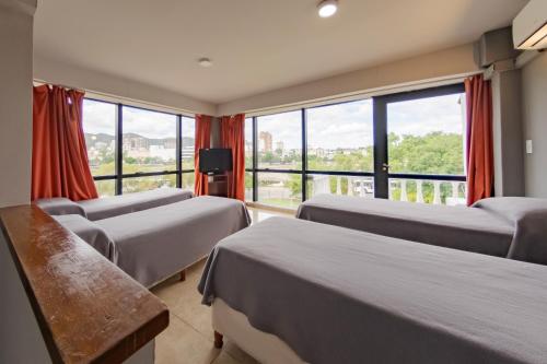 ヴィラ・カルロス・パスにあるHotel El Condadoのベッド3台と大きな窓が備わるホテルルームです。