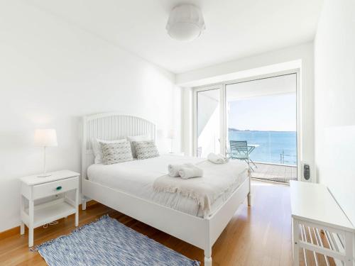 a white bedroom with a bed and a large window at Akicity Jamor Lyra in Cruz Quebrada