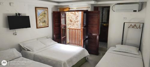 una camera da letto con due letti, una tv e una finestra di Hostal Casa de las Americas a Cartagena de Indias