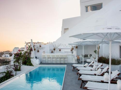 a pool with white chairs and umbrellas on a building at Canaves Sunday in Oia