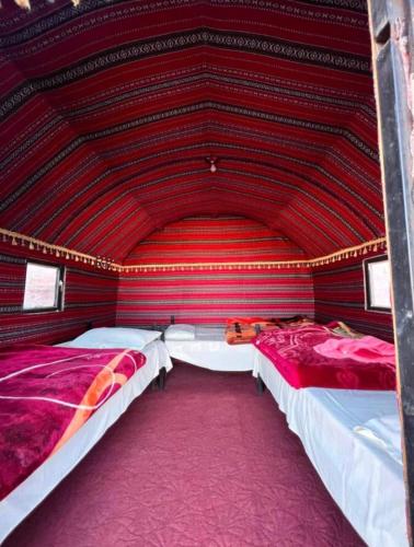 two beds in a room with a red wall at Wadi Rum Bedouin Story Camp & Tours in Wadi Rum