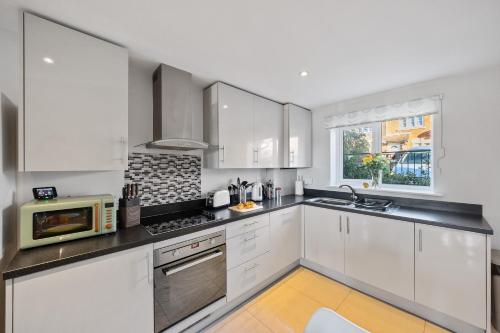 a kitchen with white cabinets and a microwave at Modern Hastings Home for Groups with Garden Terrace and Dedicated Workspace in Hastings