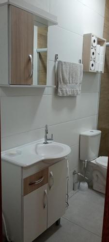 a white bathroom with a sink and a toilet at Ótima casa Jardim do Éden - Tramandaí, poucos passos do mar! in Tramandaí