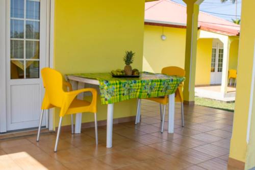 a dining room table with yellow chairs and a plant on it at Gîtes les fleurs du bananier in Goyave
