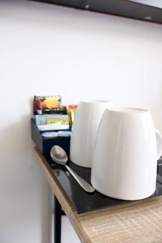 two white coffee mugs on a shelf with a spoon at Noa Hotel in Auckland