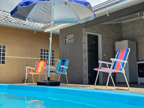 four chairs and an umbrella next to a swimming pool at Casa das Flores com piscina in Matinhos