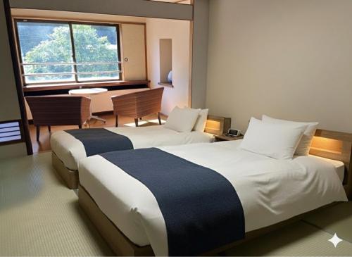 ein Hotelzimmer mit 2 Betten, einem Schreibtisch und einem Tisch in der Unterkunft 源泉の湯 福の屋 in Minakami