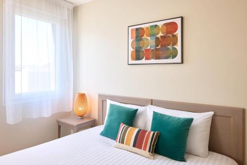 Schlafzimmer mit einem Bett mit grünen und weißen Kissen in der Unterkunft Zenitude Quality Aparthotel Le Havre les docks in Le Havre