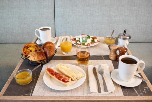 Una mesa con una bandeja de alimentos para el desayuno y tazas de café. en Zenitude Quality Aparthotel Ploërmel, en Ploërmel