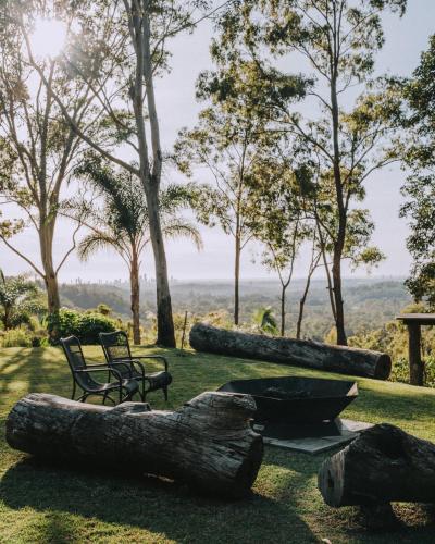 a bench and logs on the grass with trees at Nebesa Tree top villas in Mudgeeraba