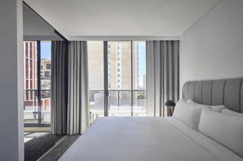a bedroom with a white bed and a large window at Meriton Suites Pitt Street, Sydney in Sydney