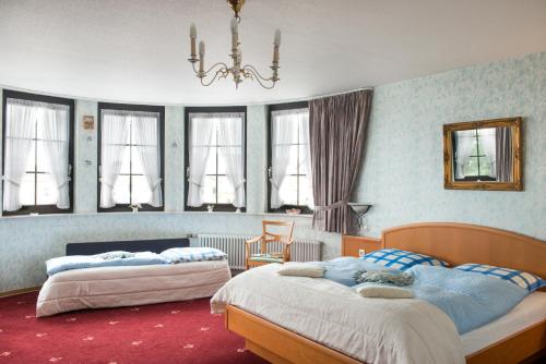 a bedroom with two beds and a chandelier and windows at Hotel zum Rehberg in Kastellaun