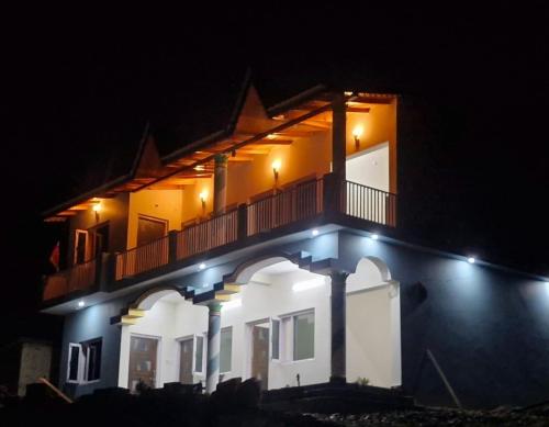DwārāhātPanchavati Hills Homestay的一座在晚上带阳台的建筑