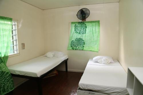 two beds in a small room with green curtains at Samoa Home in Vaitele