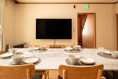 un grande tavolo da pranzo con sedie e televisore di 緑の夢の家 a Furano