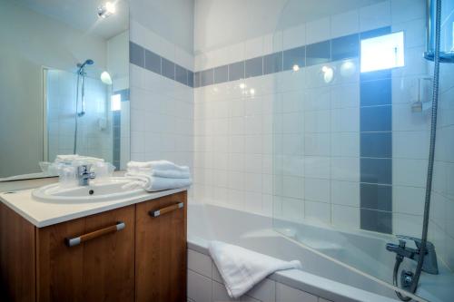 La salle de bains est pourvue d'un lavabo, d'une baignoire et d'une douche. dans l'établissement Zenitude Hôtel-Résidences Les Portes de l'Océan, à Saint-Nazaire
