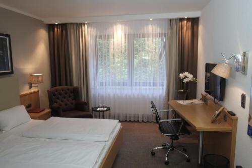 Cette chambre comprend un lit, un bureau et une fenêtre. dans l'établissement Hotel Brunnenhof International, à Wedemark