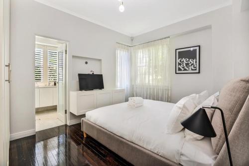 a white bedroom with a bed and a television at Henrietta's Gem - Close to cafes, shops and more in Sydney